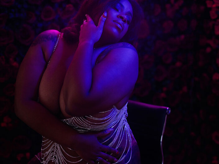 A woman in diamonds, posing in pink and blue lights.